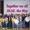Photo of girls on stage with sign saying "Together we all P.A.V.E. the Way." © GSUSA. All rights reserved.