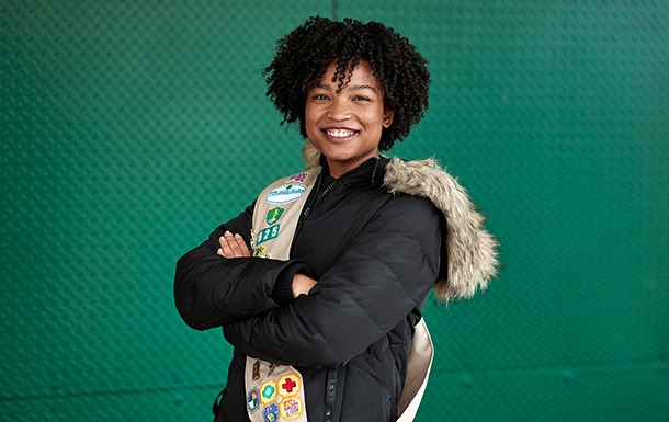 Senior Girl Scout smiling in front of a green metal wall with her arms crossed.