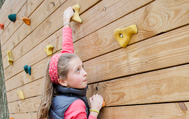 a girl climbing a wooden climbing wall with colorful climbing holds