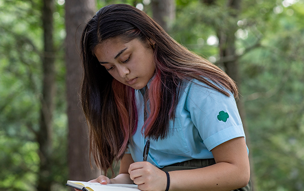 Girl sitting in the woods writing in a journal