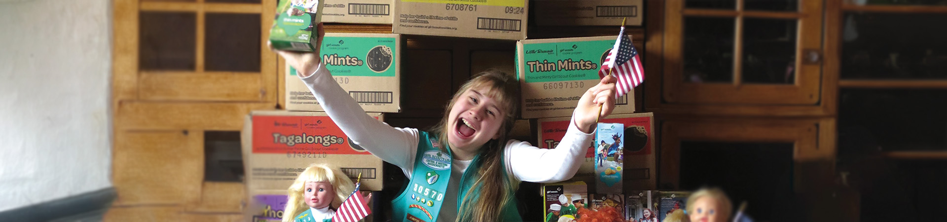  A girl sitting on a cookie throne holding an American flag and a box of Thin Mints 