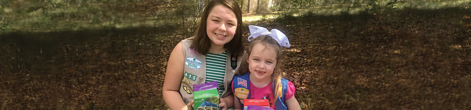  Two girl scouts smiling and holding cookie boxes. 