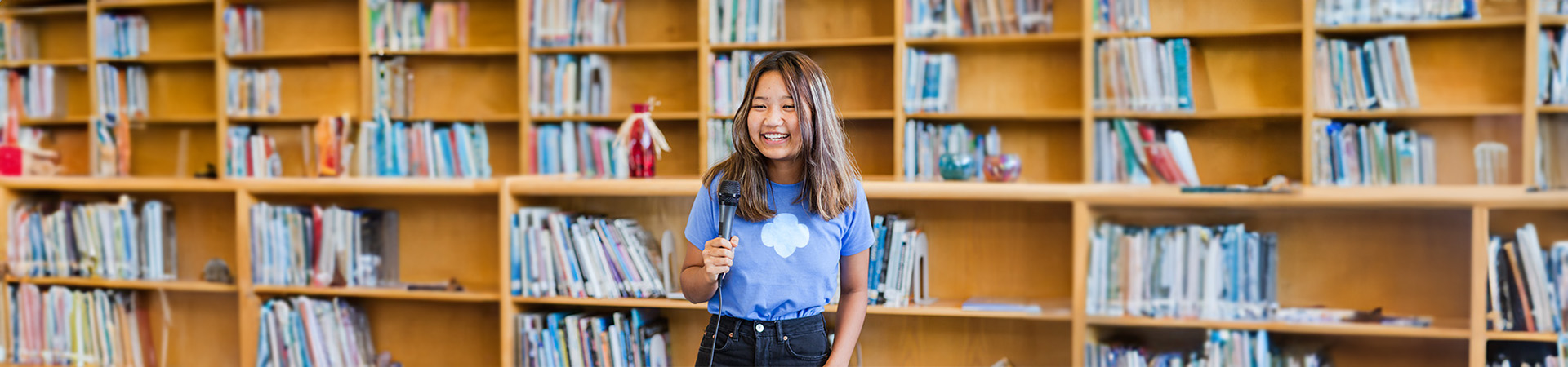  Una Girl Scout Senior parada en una biblioteca sosteniendo un micrófono 